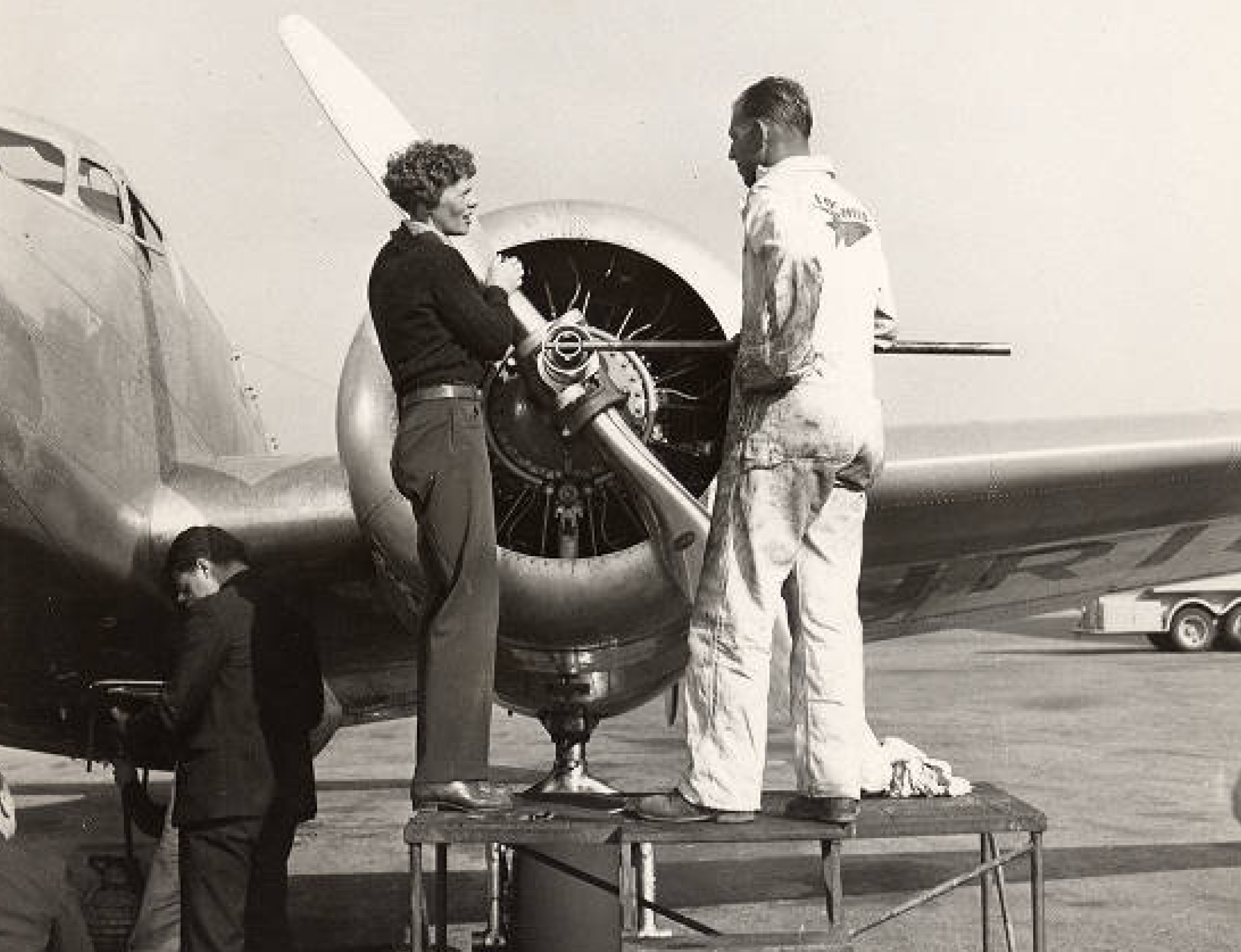 Amelia Earhart standing beside her Lockheed Electra 10E aircraft with a man in a white jumpsuit.